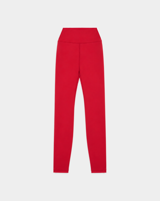A woman stands against a white background wearing the Bonnie Signature Logo Legging in Ruby, paired with a matching sports bra and yellow and black sneakers. These opaque workout leggings deliver a supportive fit for any fitness routine.