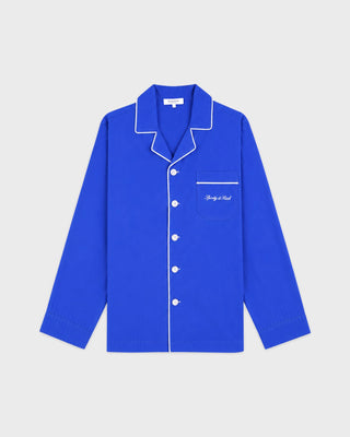 A royal blue long-sleeve pajama shirt with white piping and white buttons, featuring a chest pocket with white script embroidery, displayed on a light gray background.