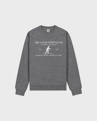 A heather gray crewneck sweatshirt with a white graphic print on the chest reading 'SKI & COUNTRY CLUB' and 'SPORTY & RICH MADE IN USA' with a skier illustration, shown on a light gray background.