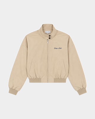 Gora Signature Logo Brighton Jacket - Taupe featuring a stand-up collar, side pockets, black Sandy Li embroidery on the chest, and a cropped boxy fit for a modern silhouette.