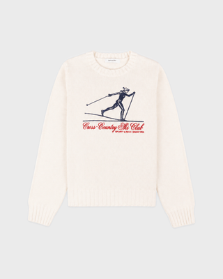 An off-white knit crewneck sweater featuring a vintage-style graphic of a skier in navy blue with red text reading 'Cross Country Ski Club' and 'SPORTY & RICH SINCE 1994' on the chest, displayed against a light gray background.
