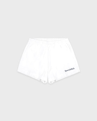 The Lucy Serif Logo Embroidered Disco Short – White is crafted from 100% cotton, featuring an elastic waistband and the Sporty & Rich logo embroidered on the lower left leg, making it perfect as a sporty lounge short. Shown here against a gray background.