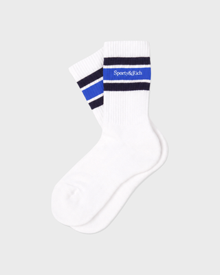 A pair of white crew socks with navy and blue stripes near the cuff, featuring the 'Sporty&Rich' brand name printed on the front, set against a solid light gray background.
