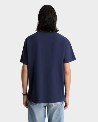 Individual with long dark hair wearing the Paris Marathon T-Shirt in navy/white and light blue jeans, viewed from the back against a plain background.
