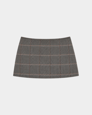 Woman wearing the Astrid Signature Logo Folding Skirt in brown check with a cropped plaid zip-up jacket, standing against a plain white wall.