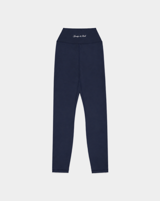 A woman is wearing the Bonnie Signature Logo Legging in Dark Navy with a supportive fit sports bra and sneakers, standing against a plain white background.