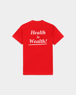 Woman in a ruby Cameron Health is Wealth T-shirt and blue jeans stands against a plain white background.