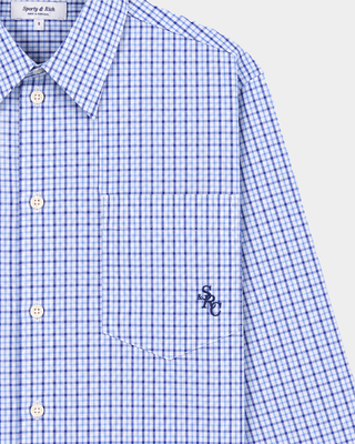 Coco SRC Oversized Shirt - Blue Mini Check features a blue and white mini check pattern in a long-sleeve, button-up, oversized silhouette with a collar. Crafted from breathable poplin for a relaxed fit, the shirt is displayed laid flat on a white background.