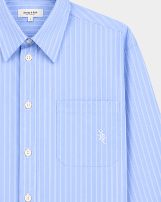 The Coco SRC Oversized Shirt - Blue Striped features a light blue, long-sleeve, button-up design with white vertical stripes and a chest pocket. Crafted from breathable poplin for a relaxed fit, it’s shown laid flat.