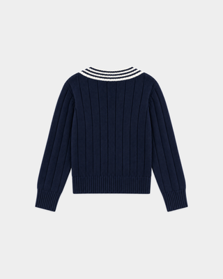 Person with braided hair in the Item SRC Cricket Sweater in Dark Navy/Off White and a white skirt, shown from behind against a plain background.