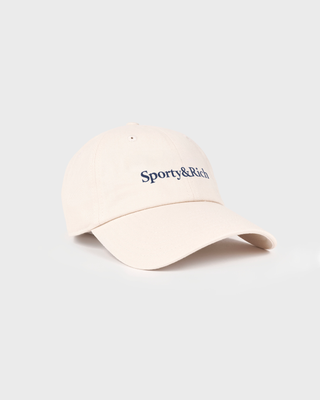 A light beige baseball cap with 'Sporty&Rich' embroidered in navy blue on the front, set against a solid light gray background.