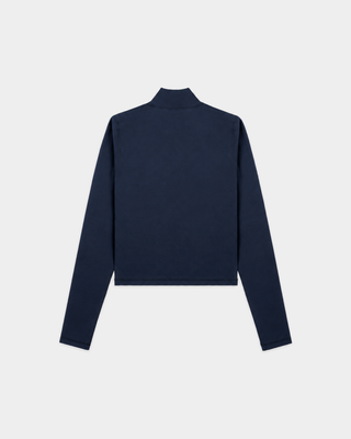 A woman in glasses wears the Freya Signature Logo Sports Jacket in Dark Navy, crafted from technical stretch fabric, paired with light gray sweatpants, standing against a plain white wall.