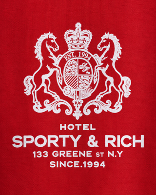 The Emmett Sr Hotel Crewneck - Ruby is a red crewneck sweatshirt inspired by vintage styles, featuring “Sporty & Rich” white logo and text on the left chest area.