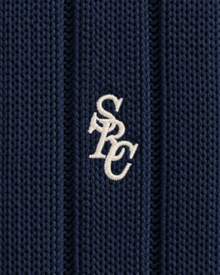 Person with braided hair in the Item SRC Cricket Sweater in Dark Navy/Off White and a white skirt, shown from behind against a plain background.