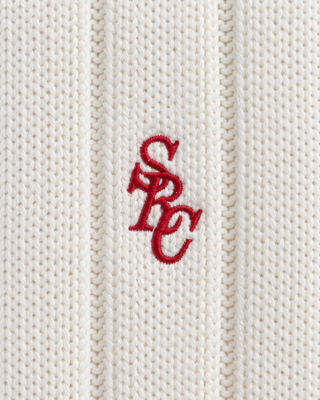 Person with braided hair wears the Item SRC Cricket Sweater in Off White/Ruby and blue jeans, facing away from the camera.