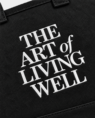 Maya Art OG Tote in black washed canvas, featuring the text THE ART of LIVING WELL printed on the front.