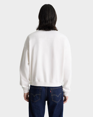 Person with long dark hair wearing the H&W Crest Embroidered Quarter Zip in White/Navy and dark blue jeans, seen from the back.