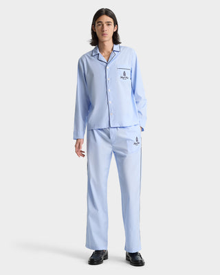 Person wearing Vendome Pyjama Pants in Ciel/Navy, featuring light blue cotton fabric, navy trim and logo, with an elastic waistband, standing against a plain white background.