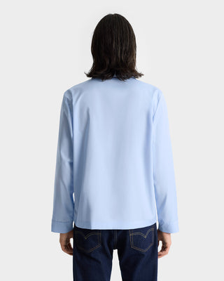 Person with shoulder-length hair wearing the Vendome Pyjama Shirt - Ciel/Navy, made in Portugal, paired with dark jeans, shown from the back.