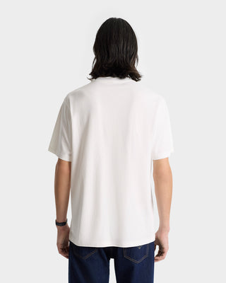 Individual with shoulder-length dark hair, seen from the back, wearing the H&W Crest T-Shirt in White/Navy (100% cotton) paired with dark jeans.