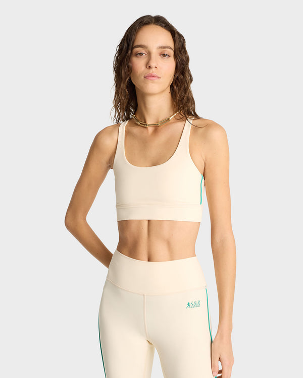 A woman models the SR Runner Active Bra in Cream/Spring Green, standing with one arm relaxed against a plain background, highlighting its great support and luxurious feel.