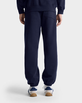 Person wearing Vendome Embroidered Sweatpant in navy/white, crafted from 100% cotton, shown from the back with white sneakers against a plain background. Made in Portugal.