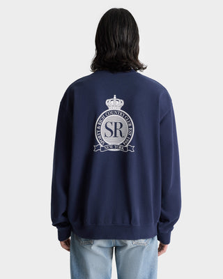 Person wearing the Royal Club Crewneck in navy/white, made from USA-grown cotton with a white emblem and back text, paired with light blue jeans.