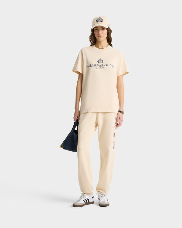 A person wearing H&W Crest Sweatpant in Cream/Navy made from USA-grown cotton, paired with a cap, holding a navy bag, and sporting sneakers.