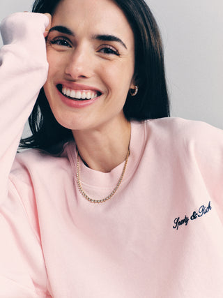 Woman smiling in a pink Syracuse Embroidered Crewneck - Pink Dolphin/Navy, made from USA grown cotton, paired with a gold chain necklace.