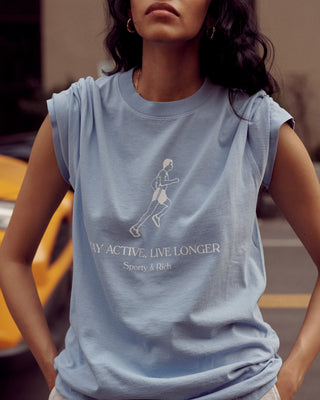 Woman in a periwinkle Live Longer T-Shirt - Periwinkle/White, made from 100% USA-grown cotton, featuring a jogging graphic and the text STAY ACTIVE, LIVE LONGER by Sporty & Rich.