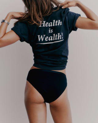 A person is seen from behind, wearing a Health is Wealth T-shirt in Navy/White made with USA-grown cotton and black underwear, standing against a plain background.