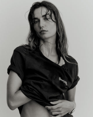 A person with wet hair poses against a white background wearing the Health is Wealth T-Shirt in faded black and white, made in the USA.
