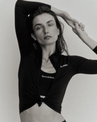 Person posing with one arm raised, wearing a black/white Serif Logo Sports Jacket made from high-quality fabric and a natural expression.