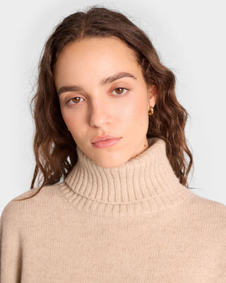 Woman with wavy brown hair wears the oversized SRC Wool Turtleneck in Cream/White, gazing calmly at the camera.