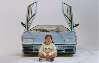 Child sitting in front of a blue sports car with open doors on a white background