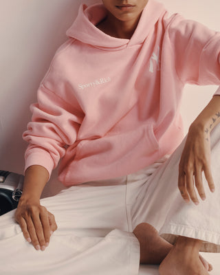 Person wearing a pink hoodie with 'Supreme' logo sitting on a white surface.