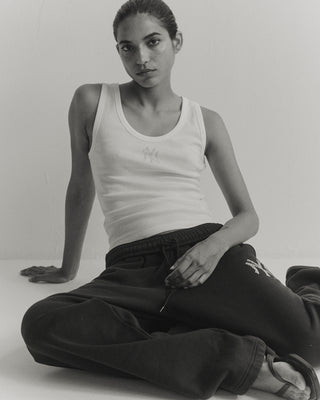 Person wearing a white tank top and black pants sitting on a light-colored floor.