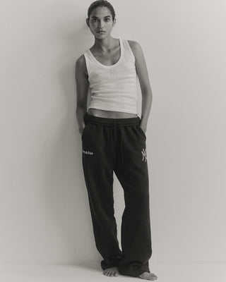 Person wearing a white tank top and black pants with visible branding against a plain background
