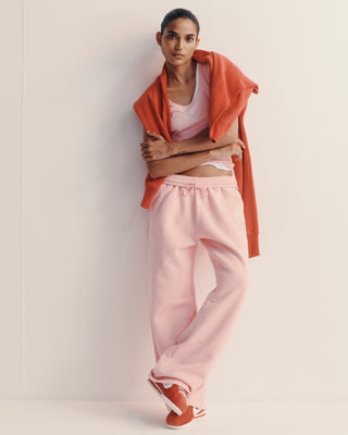 Woman wearing a peach jacket, white top, and pink pants against a light background