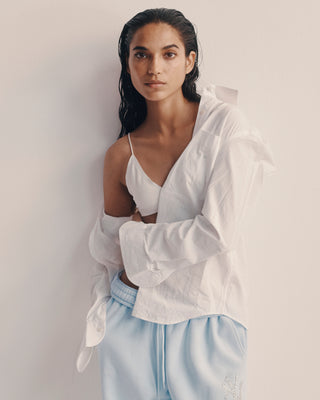 Woman wearing a white shirt and light blue pants against a plain background
