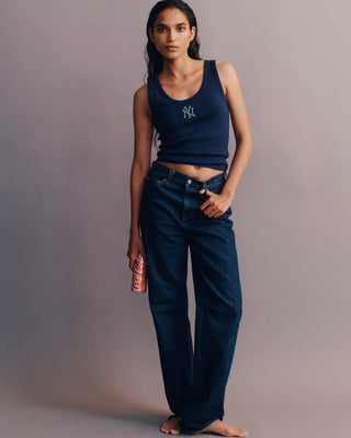 Woman wearing a navy blue tank top with a logo and dark blue jeans against a gray background