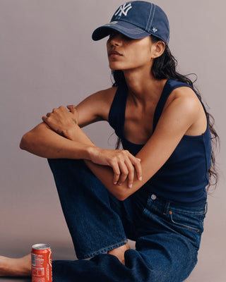 Person wearing a navy blue cap and overalls with a can of soda on a plain background