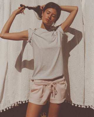 A woman posing in a light gray t-shirt and pale pink drawstring shorts against a draped white fabric backdrop.