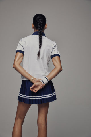 The Flint SRC 70S Pique Polo in White/Dark Navy features a crisp white piqué fabric with dark navy collar, sleeve cuffs, and piping. A small embroidered logo on the chest adds a classic 70s tennis polo vibe.