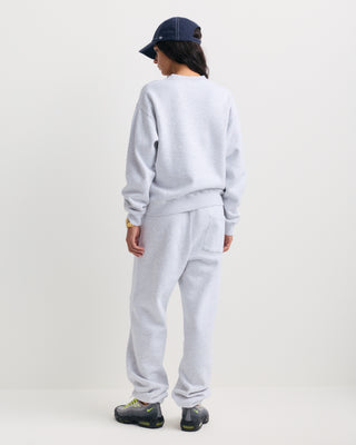 The Eeva Serif Logo Embroidered Crewneck in Heather Gray features a classic crewneck design with long sleeves and subtle white embroidered text on the left chest, making it perfect for fans of vintage-style sweatshirts.