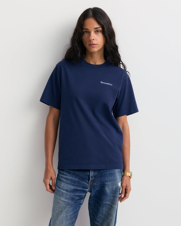 The Fema Serif Logo T-shirt in Dark Navy features a short-sleeve, unisex design with text on the left chest, crafted from 100% cotton and shown laid flat on a white background. This Sporty & Rich tee offers both comfort and timeless style for any wardrobe.