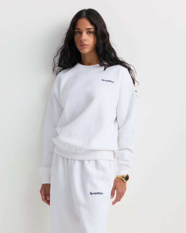 Eeva Serif Logo Embroidered Crewneck in white, inspired by vintage sweatshirts and featuring Sporty & Rich text embroidered on the left chest, displayed on a plain background.