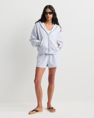 The Emaro Serif Logo Embroidered Zip Hoodie in Heather Gray is laid flat, showcasing its light gray color, zip-up front, front pockets, and a small white embroidered logo on the left chest. This super soft hoodie offers a relaxed fit for ultimate comfort.