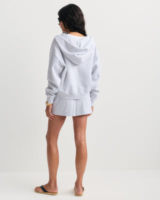 The Emaro Serif Logo Embroidered Zip Hoodie in Heather Gray is laid flat, showcasing its light gray color, zip-up front, front pockets, and a small white embroidered logo on the left chest. This super soft hoodie offers a relaxed fit for ultimate comfort.