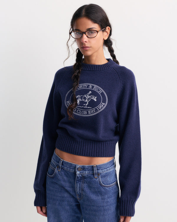 The Joconde Riding Club Knitted Boxy Sweater in Dark Navy features a modern, relaxed fit with a boxy silhouette and showcases the Sporty & Rich Riding Club Est. 1994 lettering and horse logo on the chest.